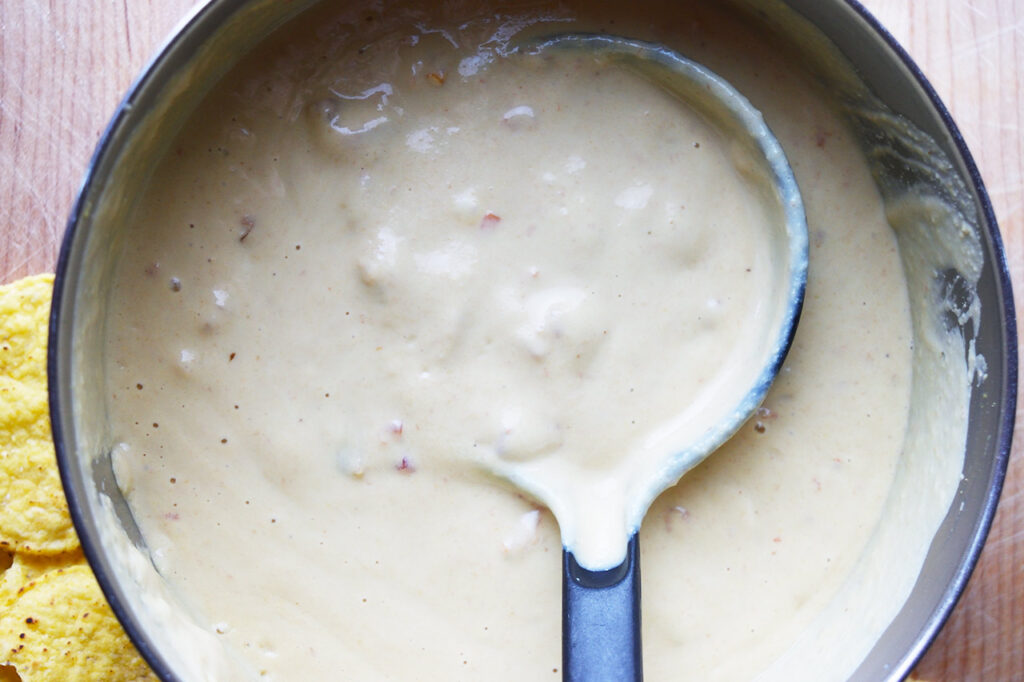 The vegan queso warmed in a pot with a ladle resting in it.