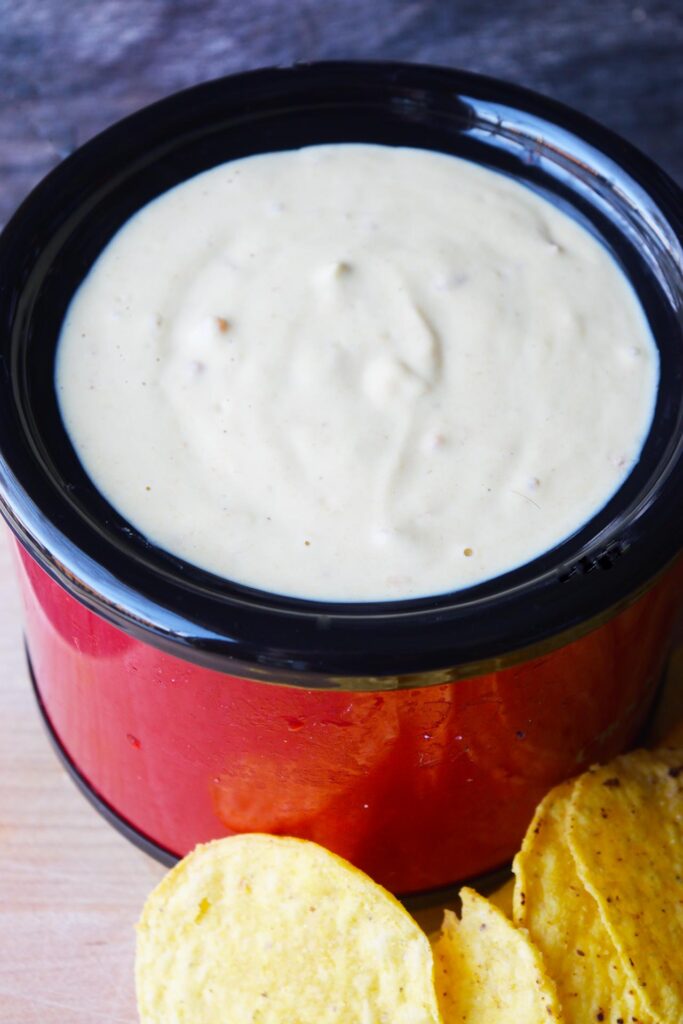 A crock of vegan queso with a few corn chips laying at the base.