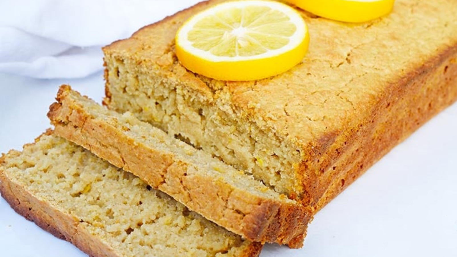 A partially cut loaf of lemon bread on a white surface.