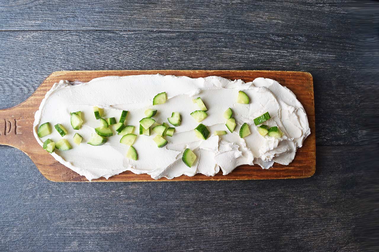 Chopped cucumbers sprinkled over cream cheese on a charcuterie board.
