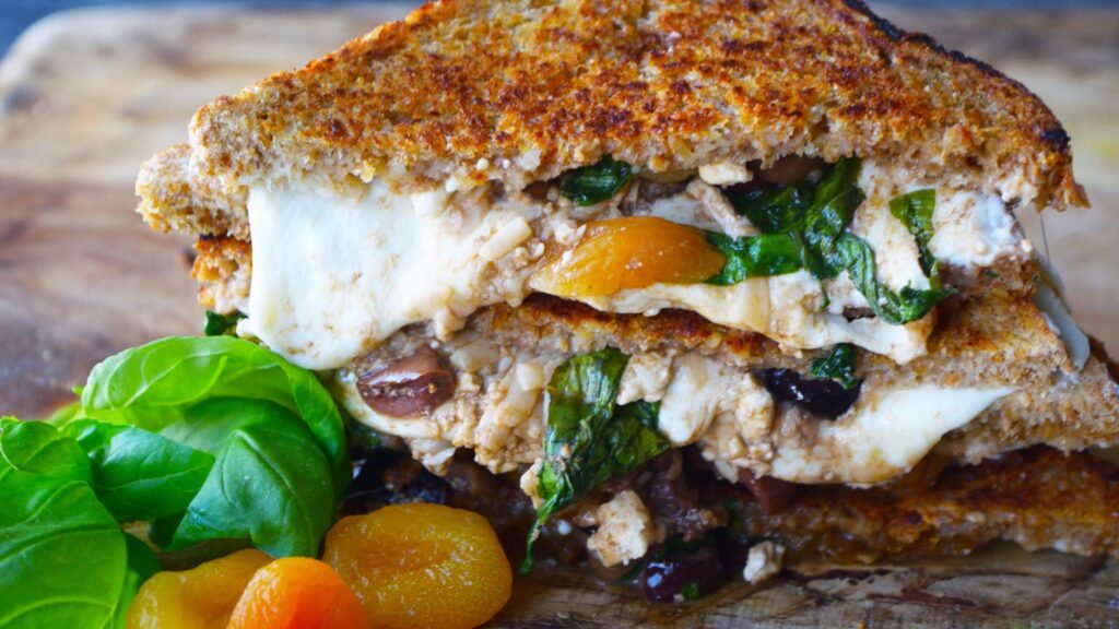 A stacked Mediterranean grilled cheese sandwich on a cutting board.