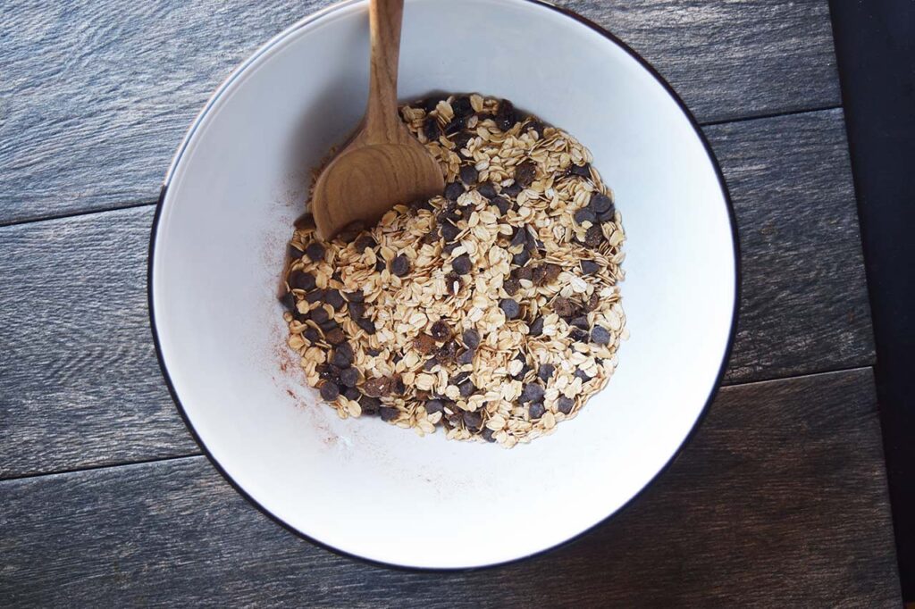 Dry ingredients for this Homemade Granola Bars Recipe in a mixing bowl with a wooden spoon.