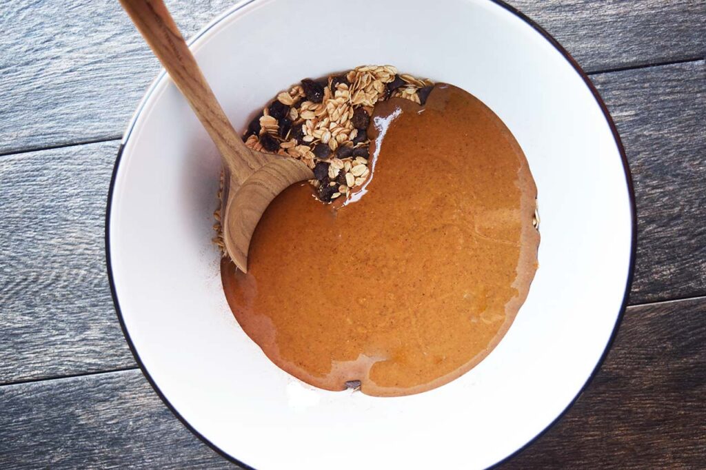 Nut butter mixture added to dry ingredients in a white mixing bowl.