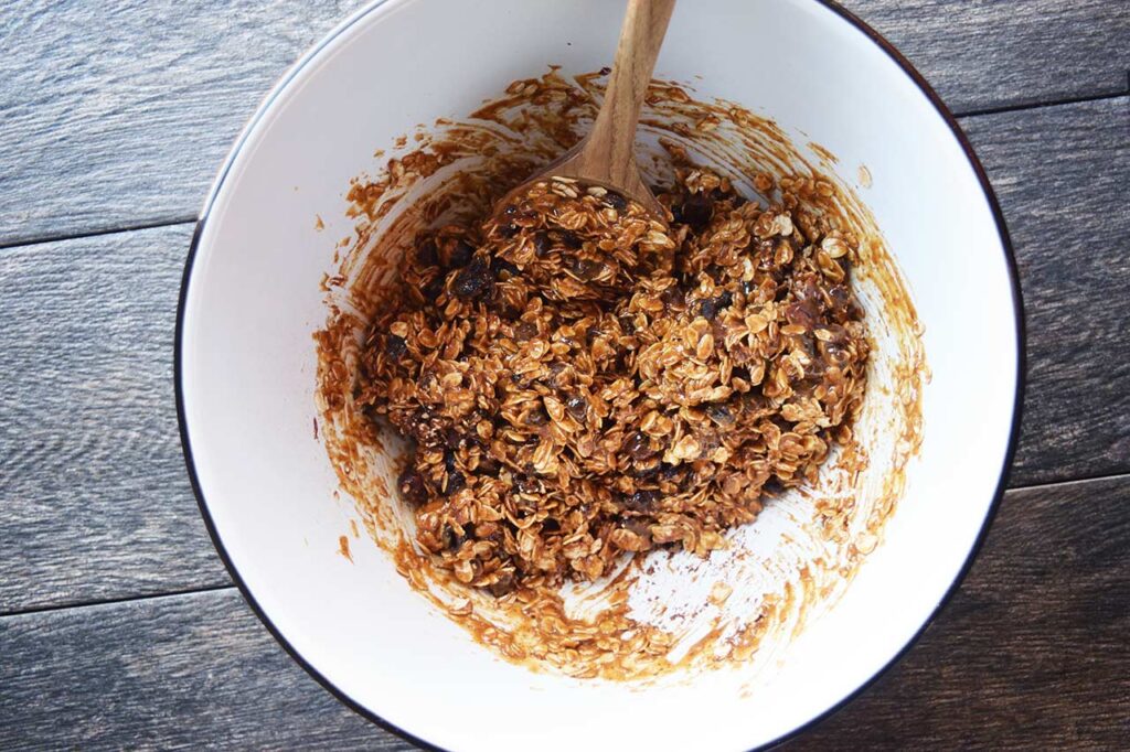 Homemade Granola Bar batter mixed in a white mixing bowl with a wooden spoon.