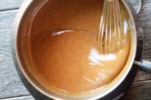 Wet ingredient being whisked in a pot on a cooktop.