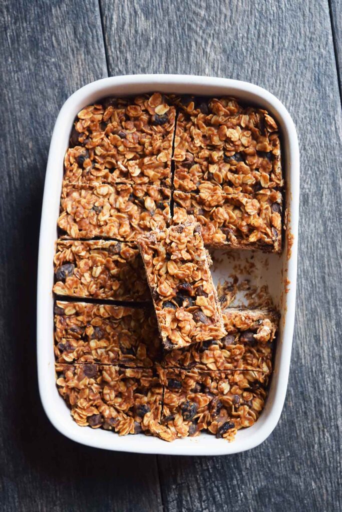 An overhead view of a white casserole dish filled with Homemade Granola Bars. One has been removed and is sitting on top of the others.