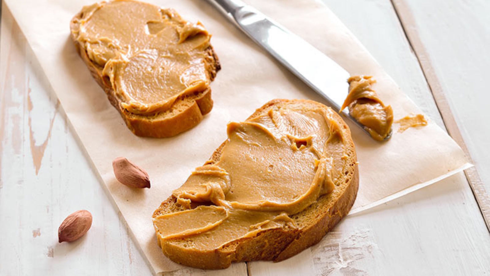 Two slices of bread on a tabletop with nut butter spread on them.