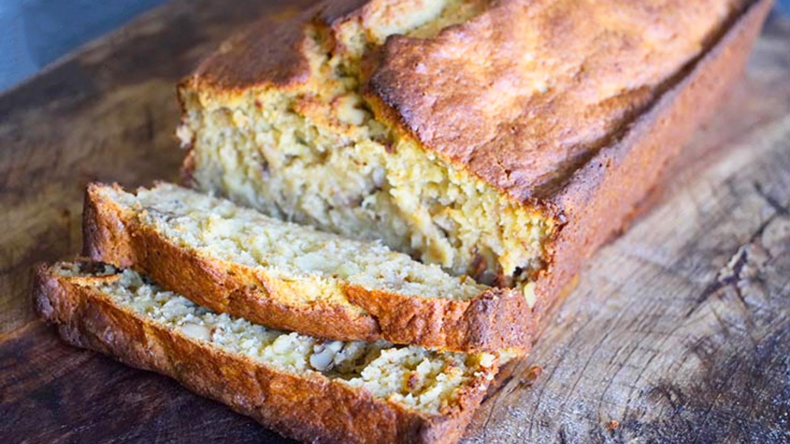 A loaf of oat flour banana bread lays partially sliced on a cutting board.