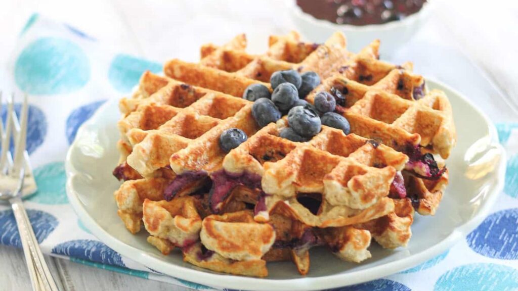 Two large oatmeal waffles on a plate with fresh blueberries on top.