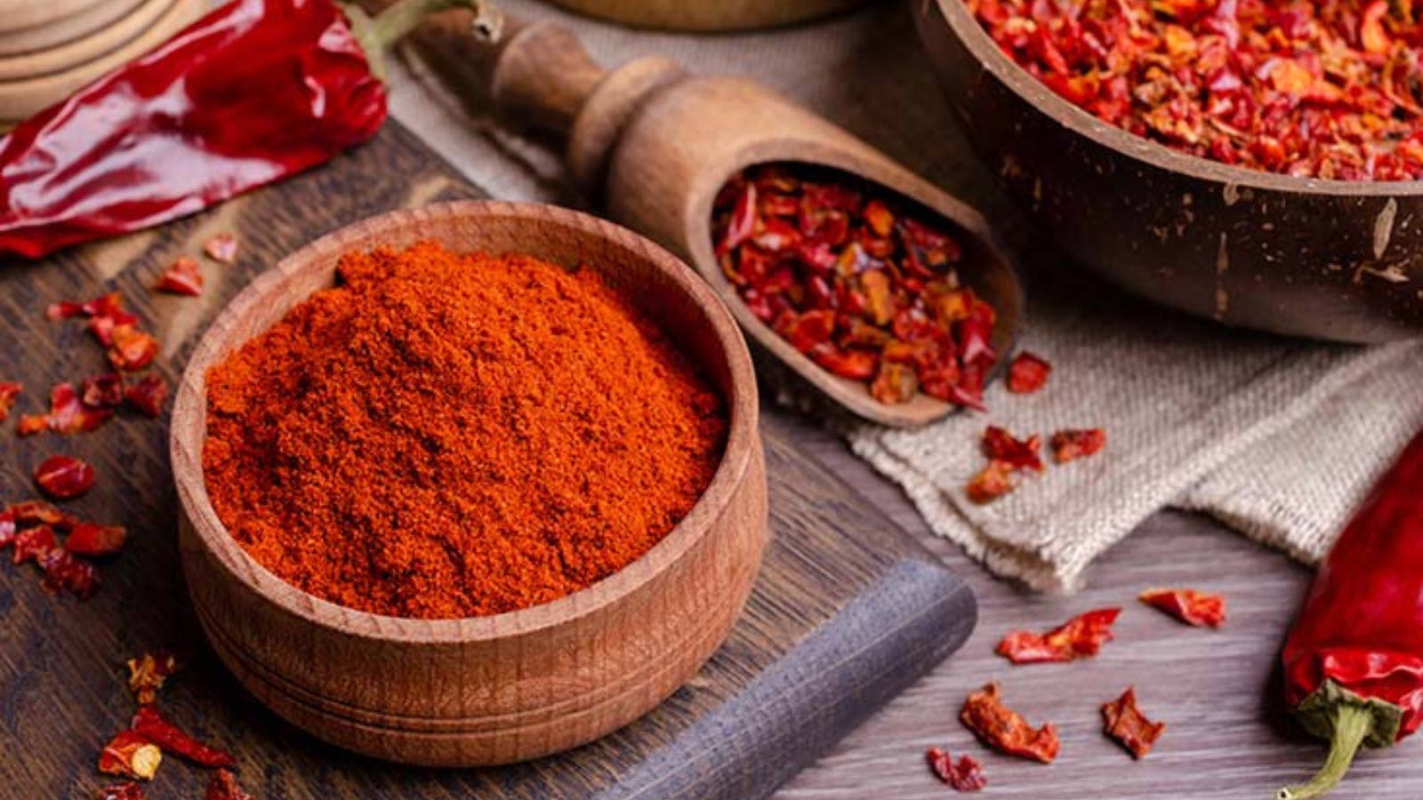 Paprika dried and ground in bowls and a wooden scoop.