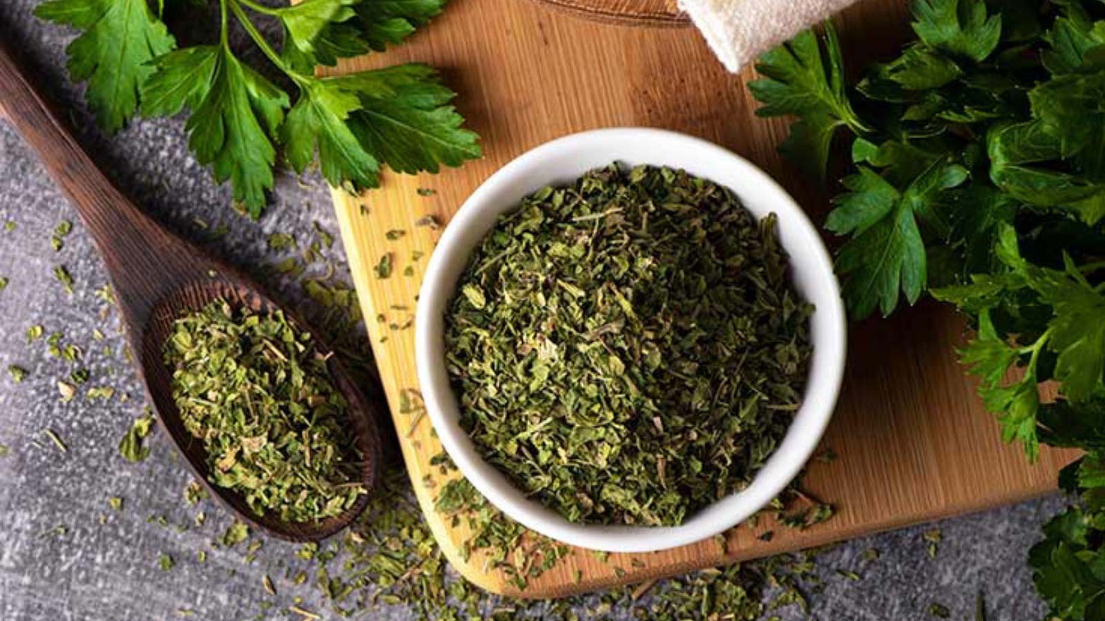 Dried parsley in a white bowl and in a wooden spoon that sits next to it.