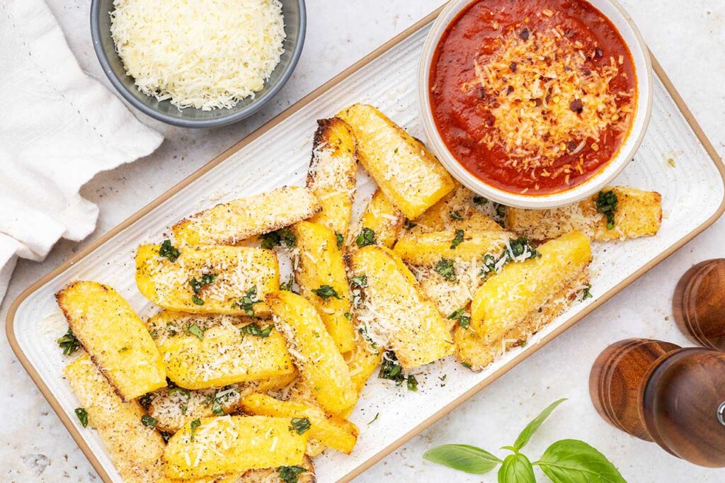 An overhead view of a platter with polenta fries and a bowl of marinara dip.