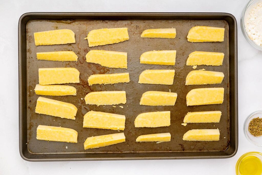 Polenta fries lined up on a baking sheet.