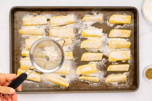 Sifting starch over the polenta fries on a baking sheet.