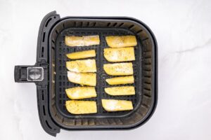 Uncooked polenta fries lined up in an air fryer basket.
