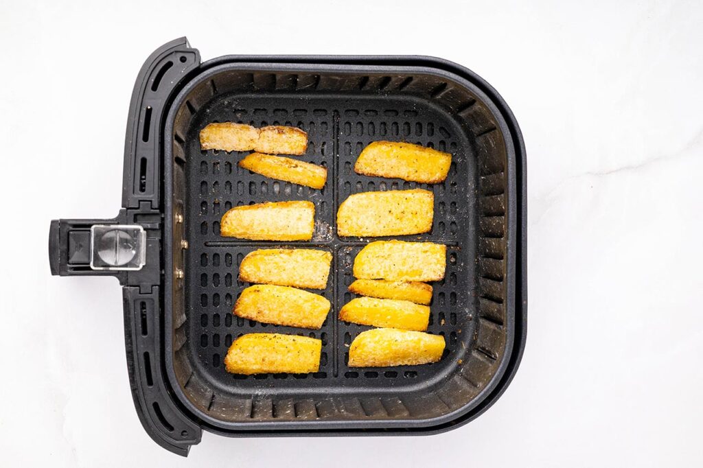 Crispy polenta fries still in an air fryer basket.