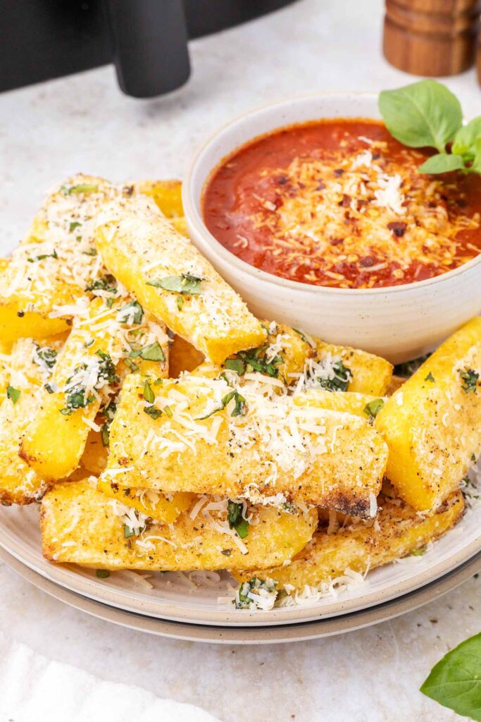 A plate filled with polenta fries and also a bowl of marinara sauce for dipping.