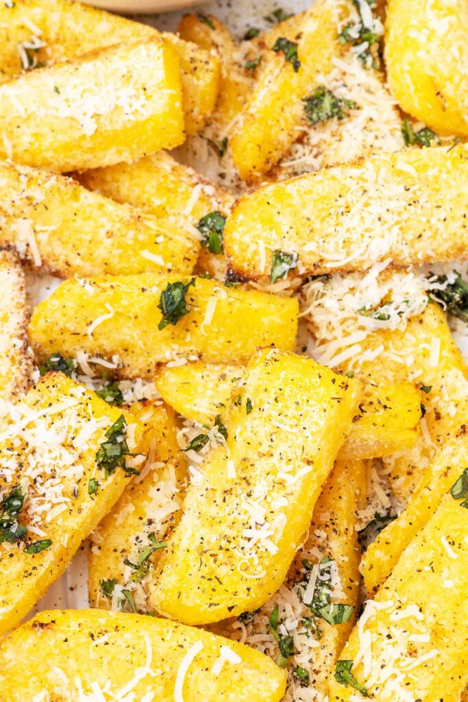 A closeup of polenta fries garnished with grated parmesan cheese.