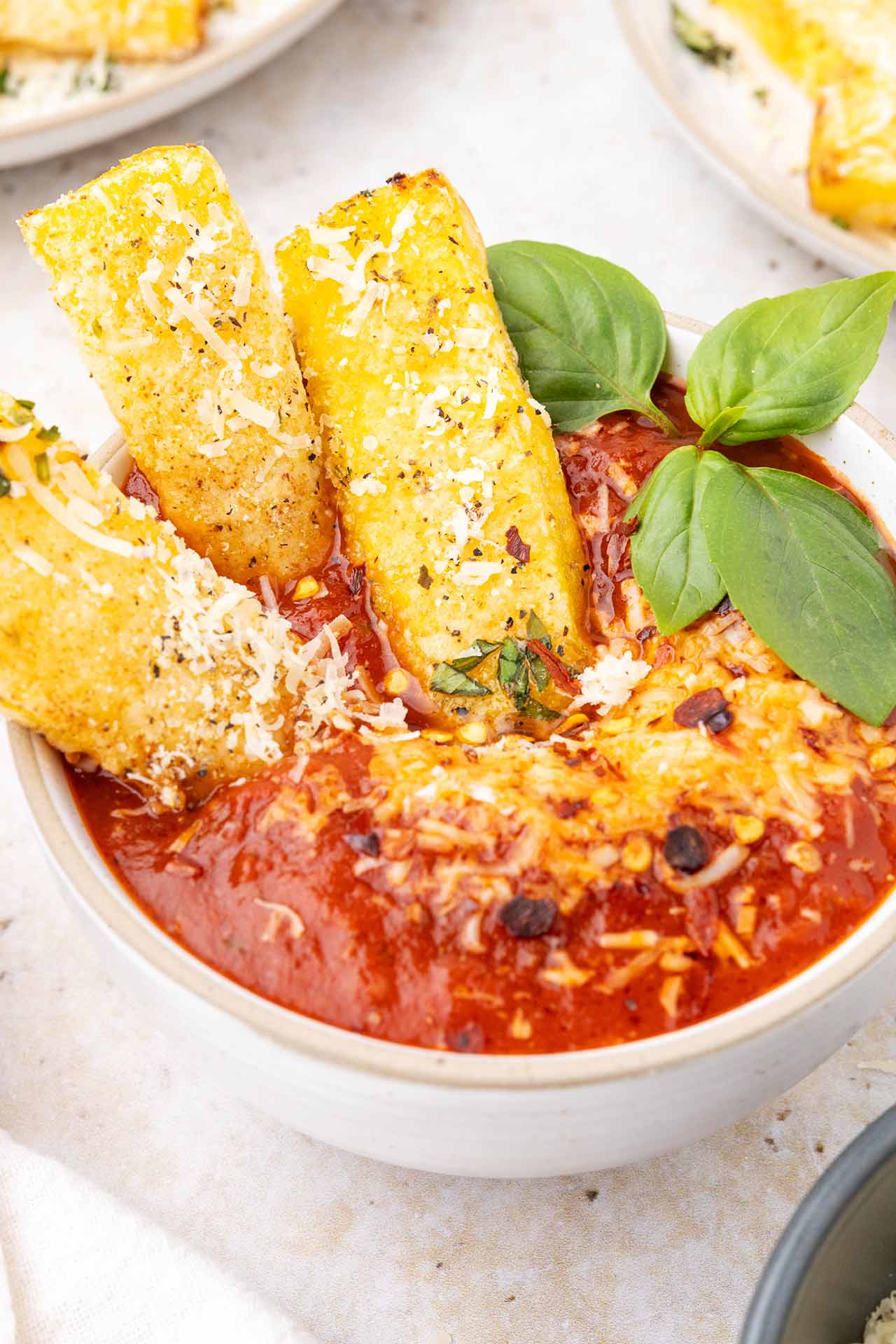 Three polenta fries sitting in a bowl filled with marinara sauce.