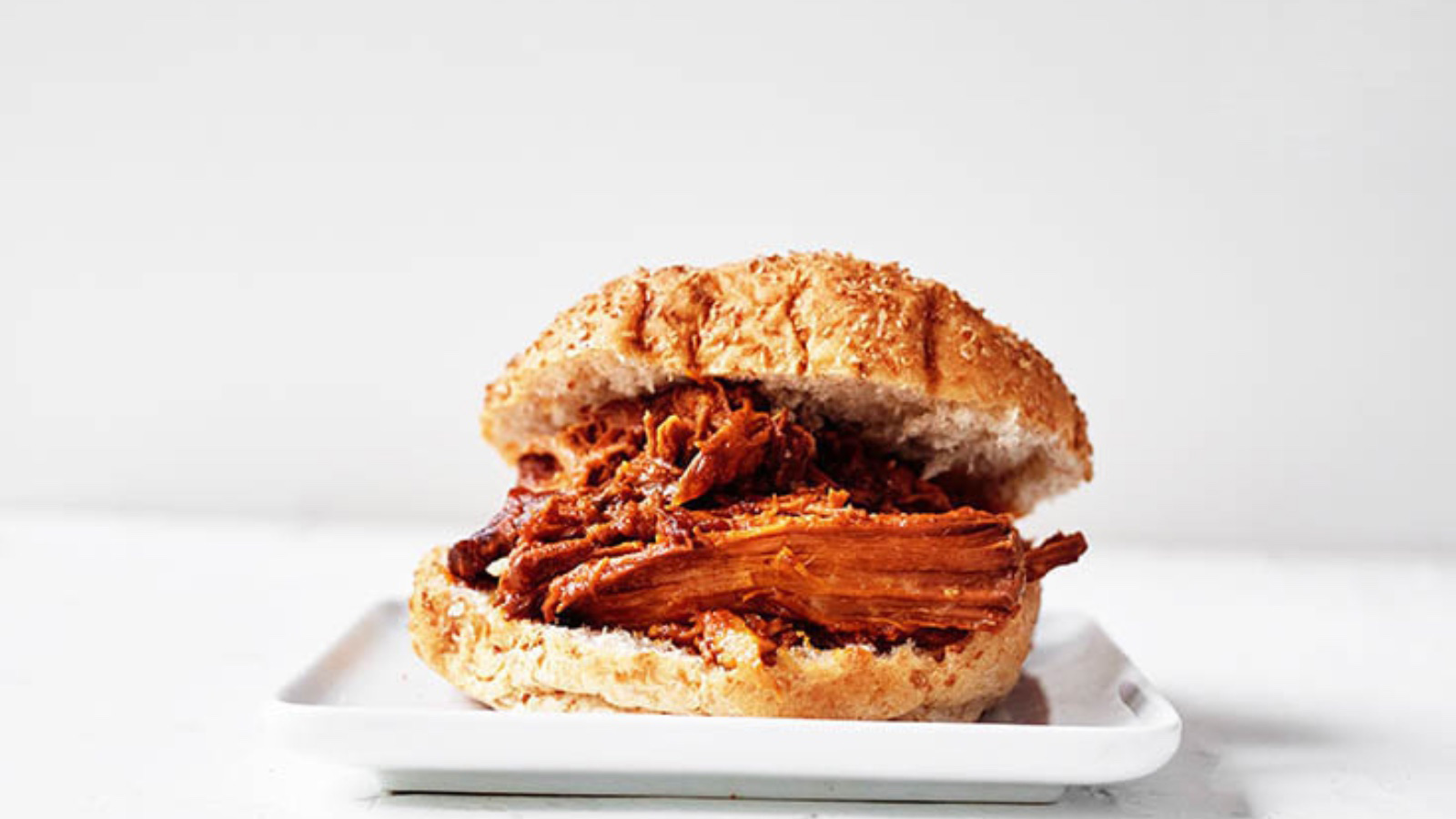 A pulled pork sandwich on a white plate on a white background.