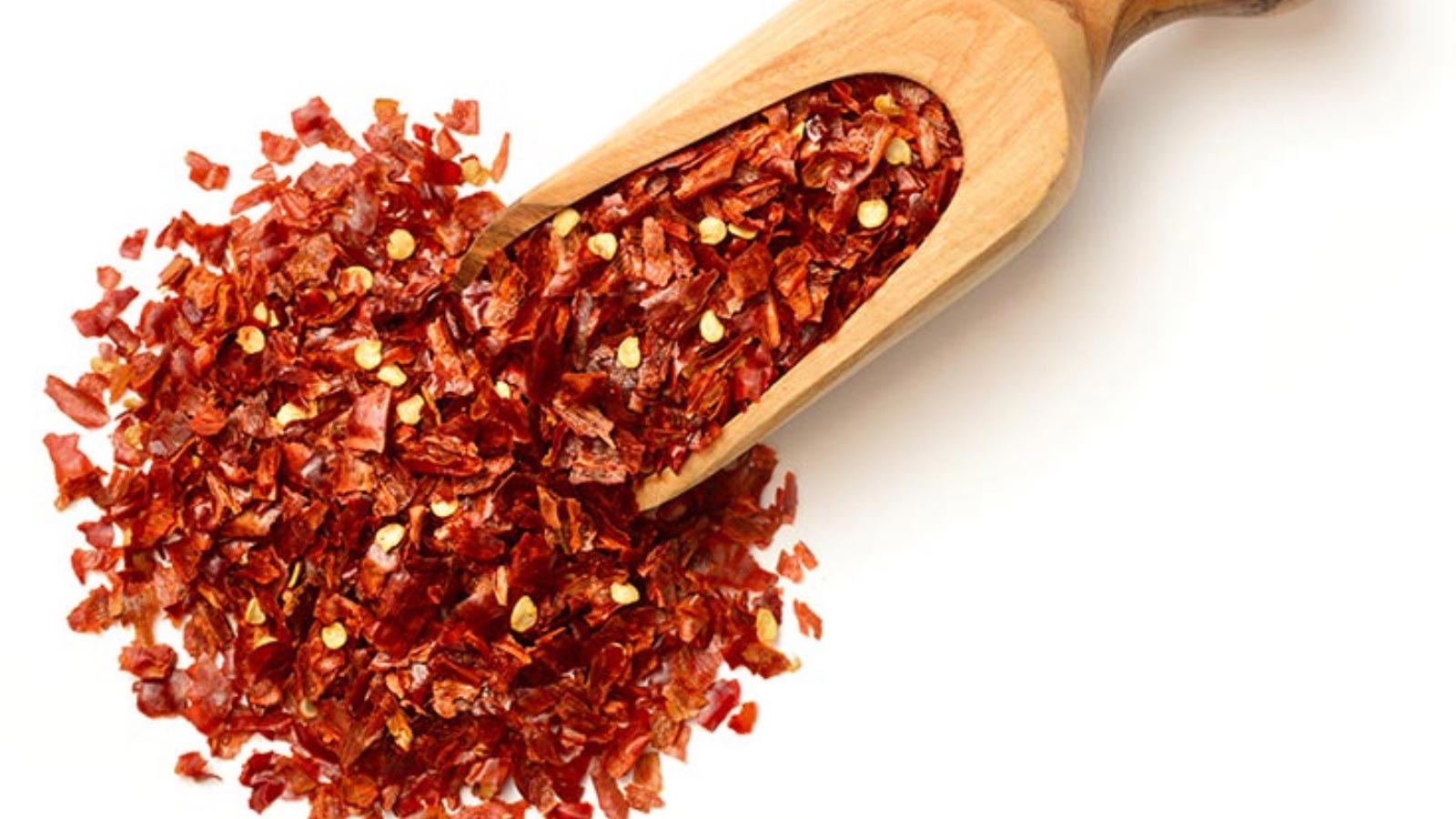 A wooden scoop filled with red chili flakes on a white background.