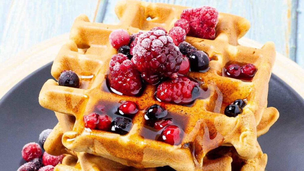 A closeup of waffles with berries and berry sauce over the top.