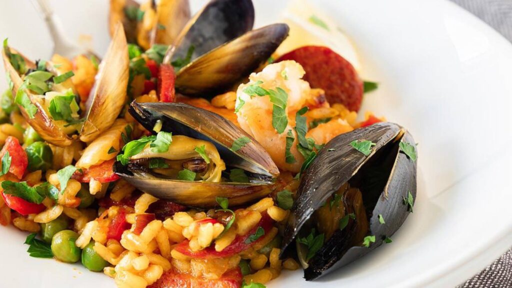 A closeup of a white bowl filled with Seafood Paella with Mussels, Shrimp and Chorizo.