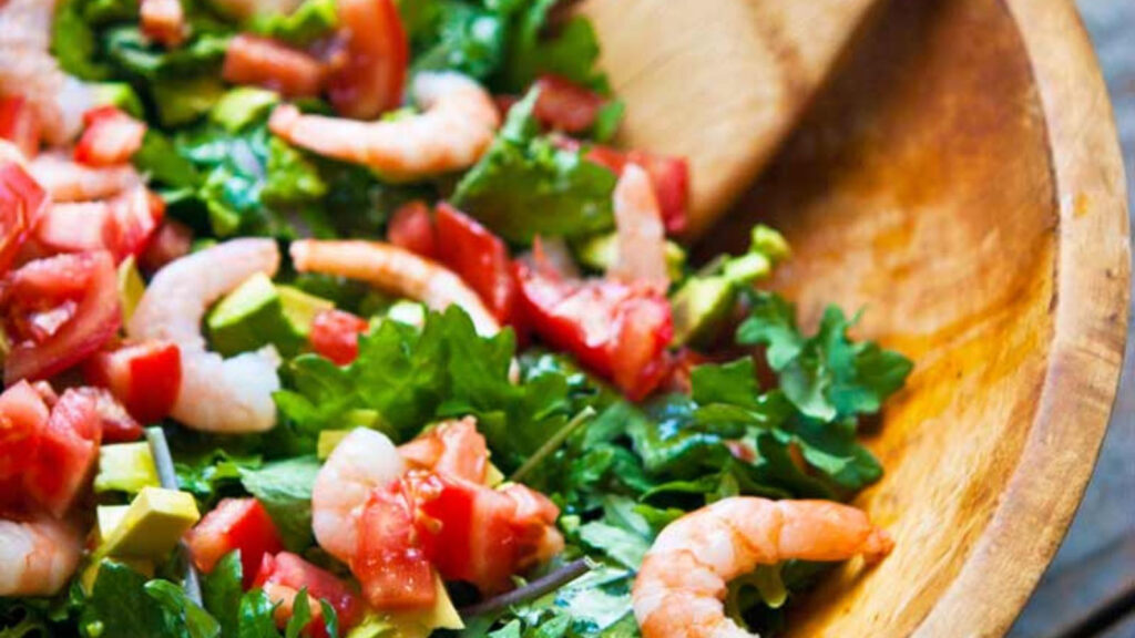 A closeup of a wood bowl filled with shrimp and kale salad.