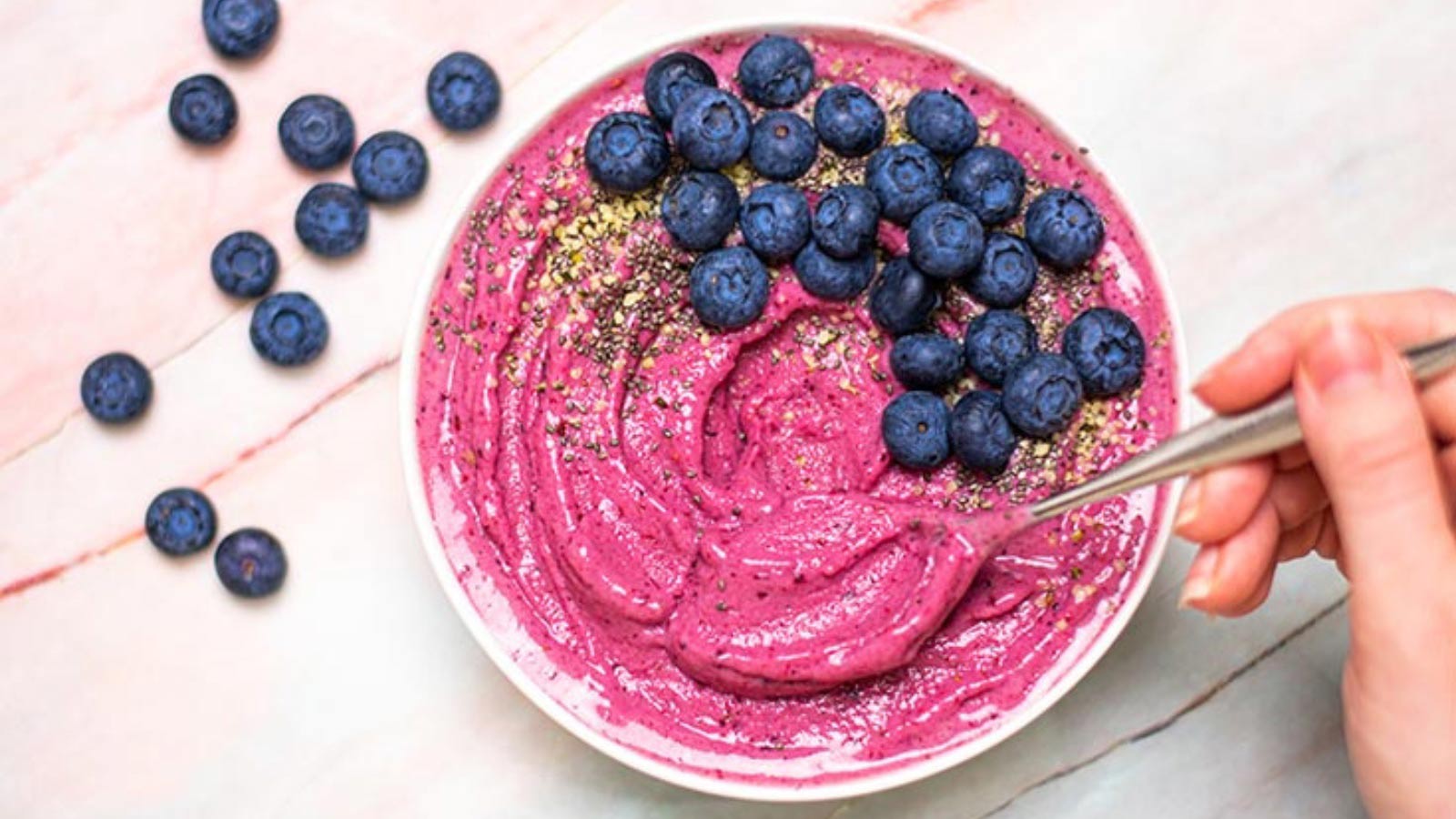 A white bowl filled with a pink smoothie, topped with fresh blueberries and chia seeds.