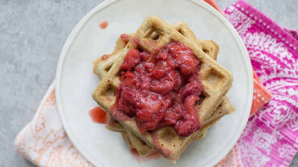 An overhead view of a stack of waffles with strawberry compote on top.