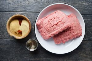 Ground turkey in a bowl, next to a smaller bowl of spices and a small container of oil.