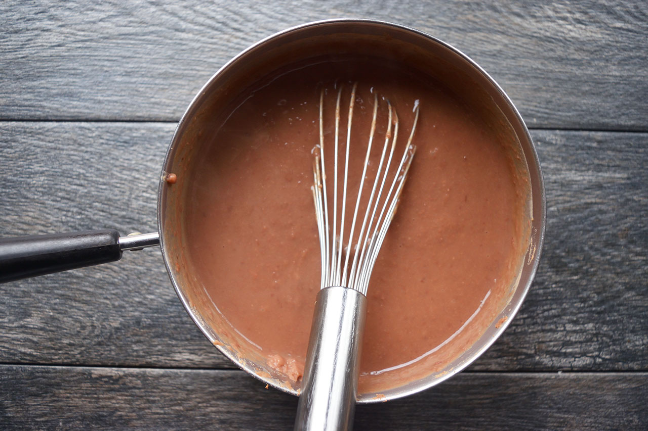 Refried beans warmed in a pot with a whisk.