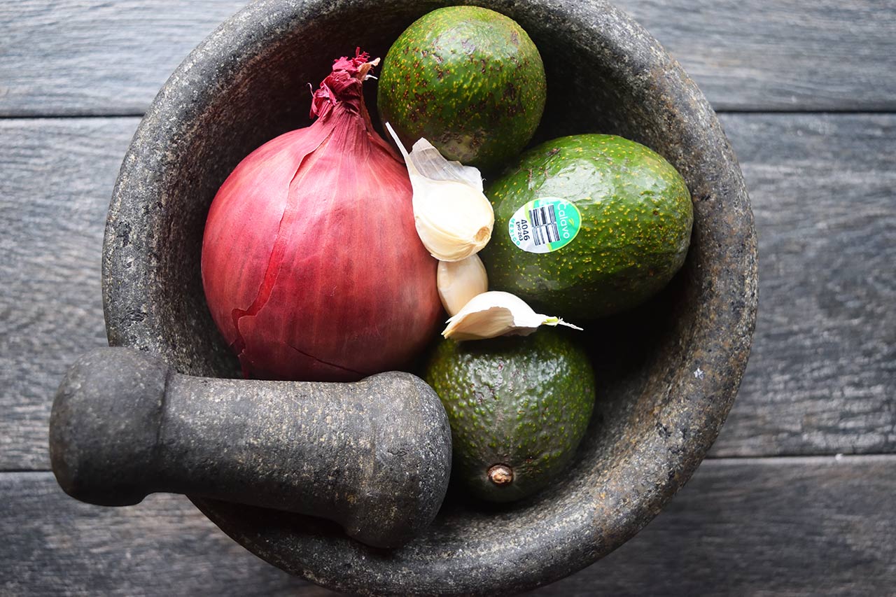Guacamole ingredients in a mortar with a pestle.