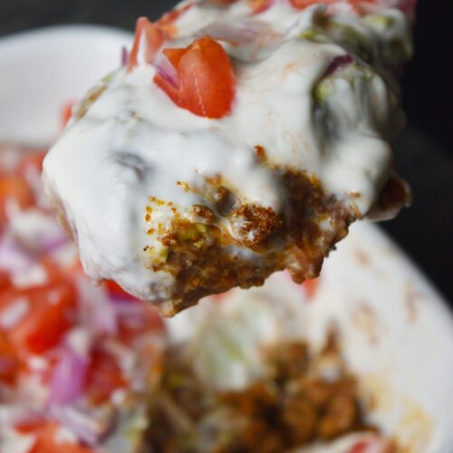 A spoon lifting up a serving of Taco Salad Casserole from a white casserole dish.