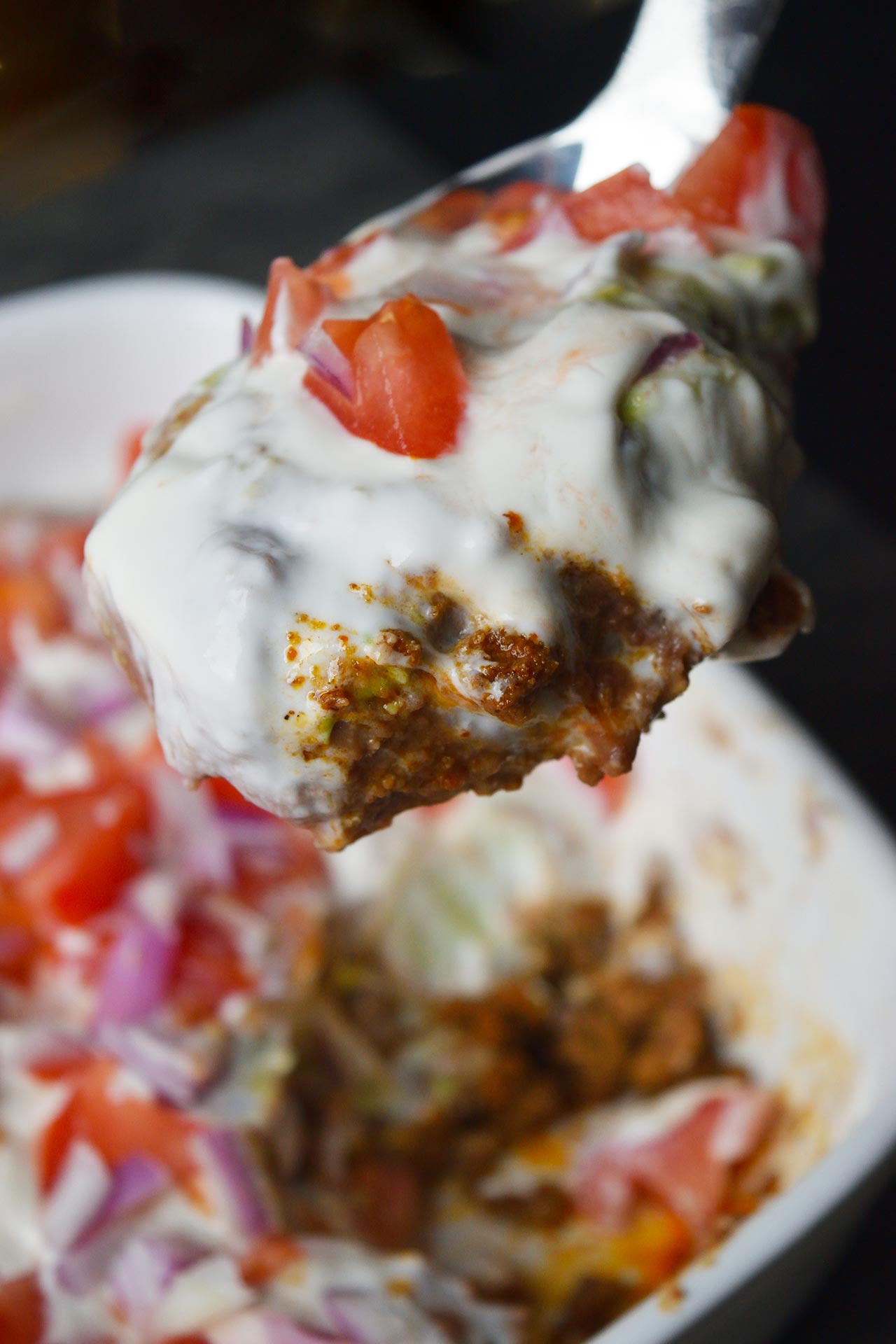 A spoon lifting up a serving of Taco Salad Casserole from a white casserole dish.