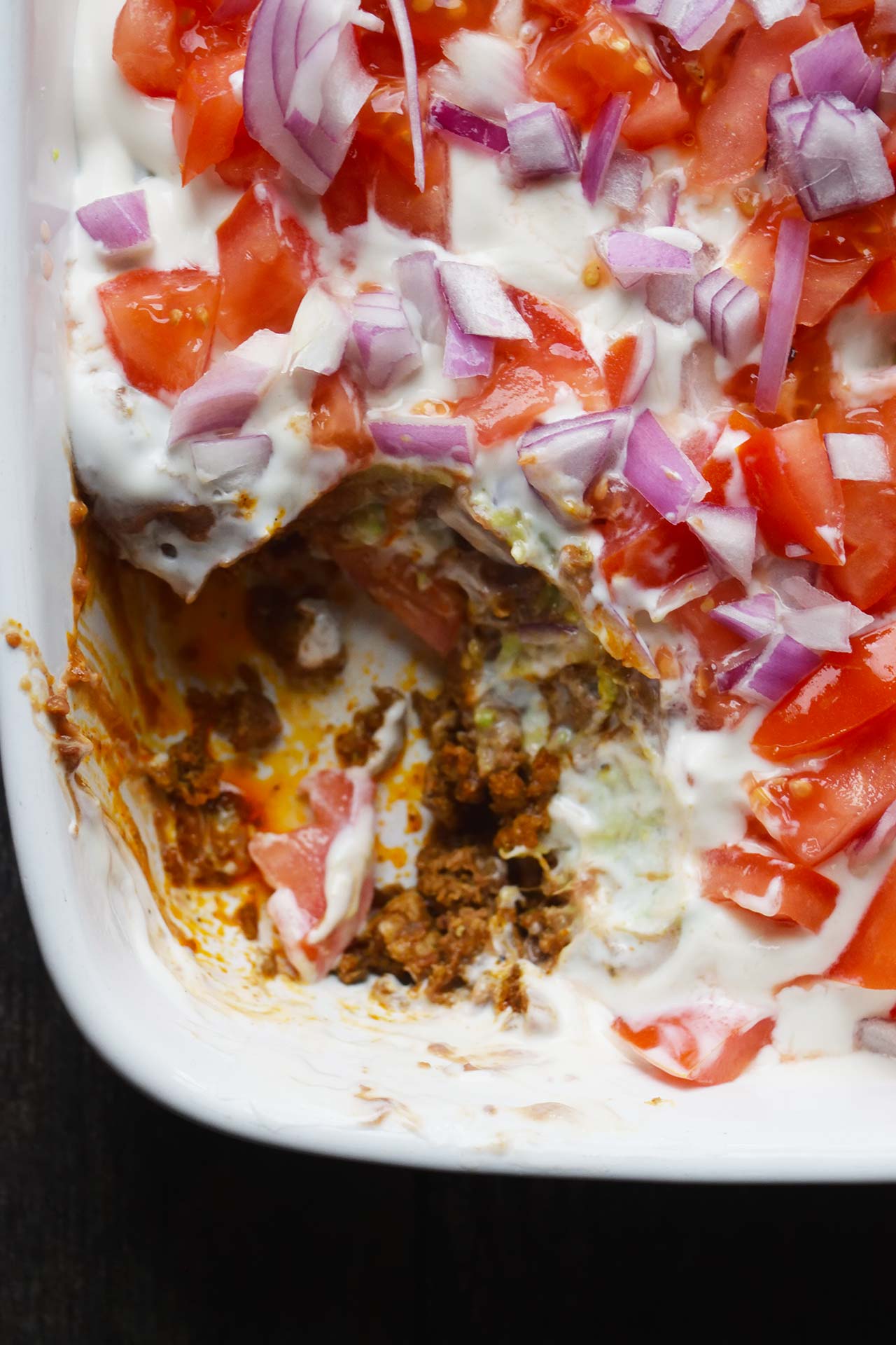 A white casserole dish of Taco Salad Casserole with a serving removed.