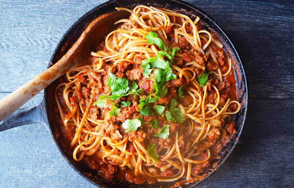 An overhead view of a cast iron skillet filled with taco spaghetti. A wooden spoon rests in the pan.