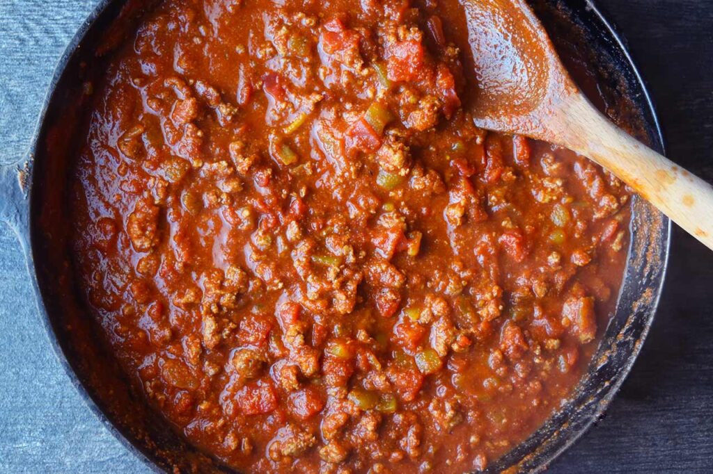 Taco spaghetti sauce simmering in a cast iron skillet. A wooden spoon rests in the pan.