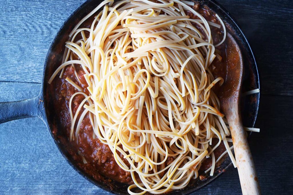 Cooked pasta added to the taco spaghetti sauce in a cast iron skillet.