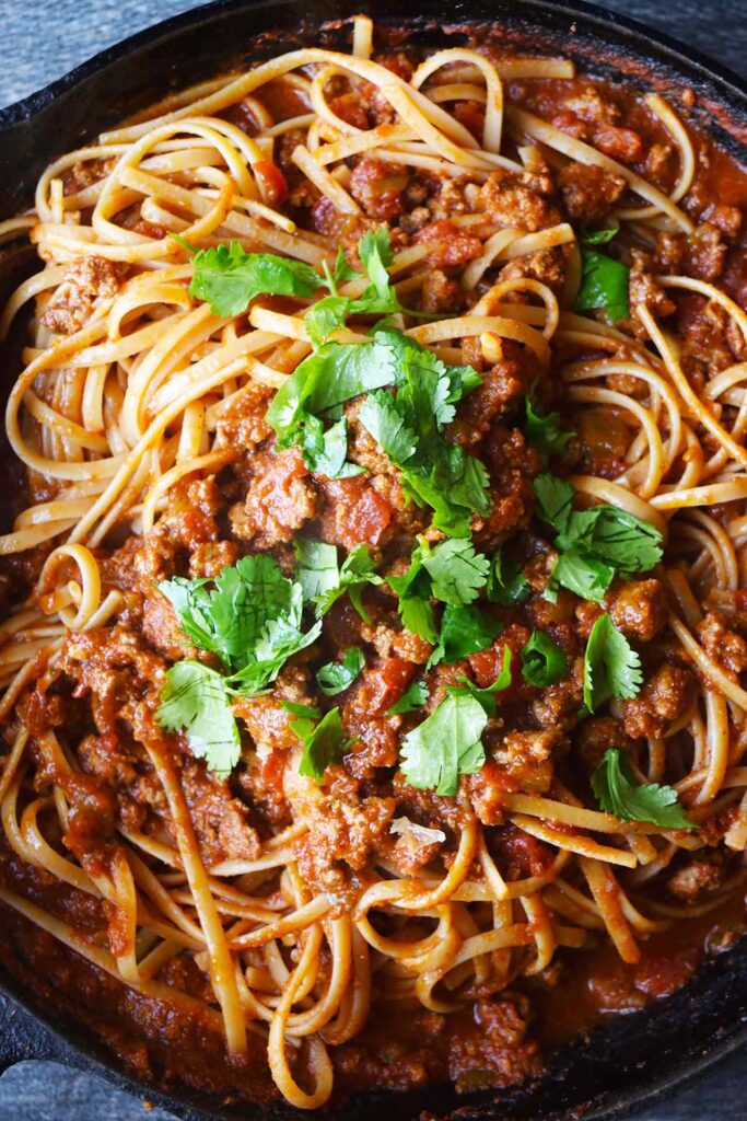 An overhead closeup of taco spaghetti in a cast iron skillet, garnished with fresh herbs.