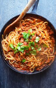 An overhead view of Taco Spaghetti in a skillet with a wooden spoon.