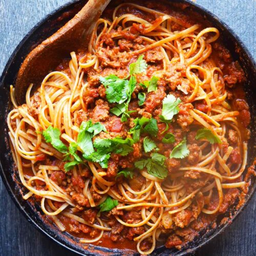 An overhead view of Taco Spaghetti in a skillet with a wooden spoon.