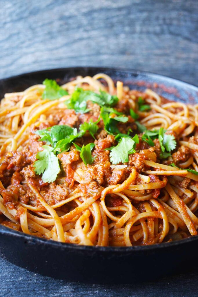 A side view of a cast iron skillet filled with taco spaghetti, garnished with. fresh herbs.