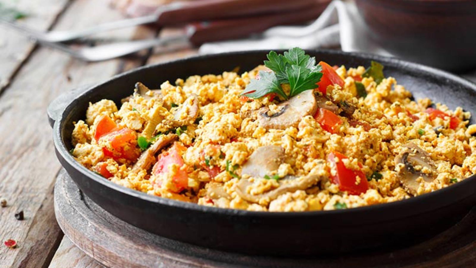 A black skillet filled with tofu scramble sitting on a wood surface.