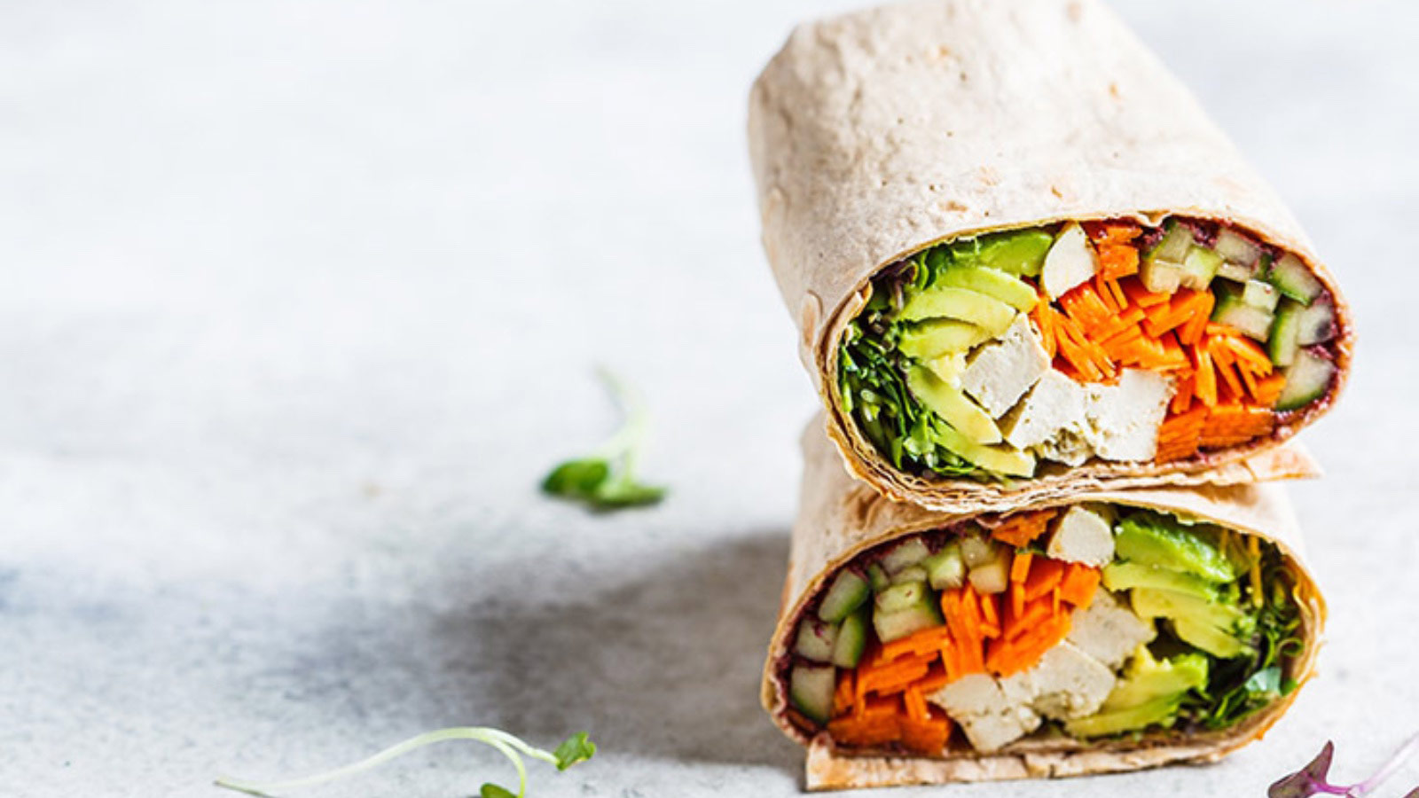 A vegan breakfast burrito stacked on a white surface.