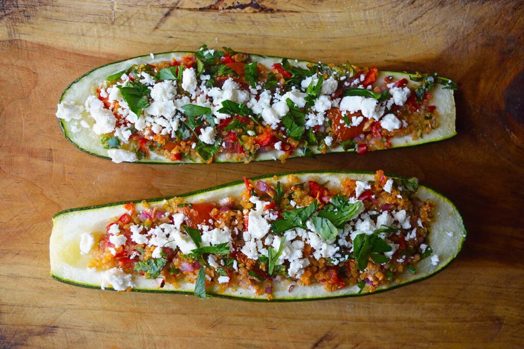 Two baked Zucchini Boats laying next to each other on a wood cutting board.