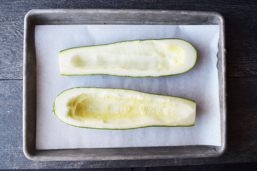 Two zucchini halves laying on a parchment-lined baking sheet.