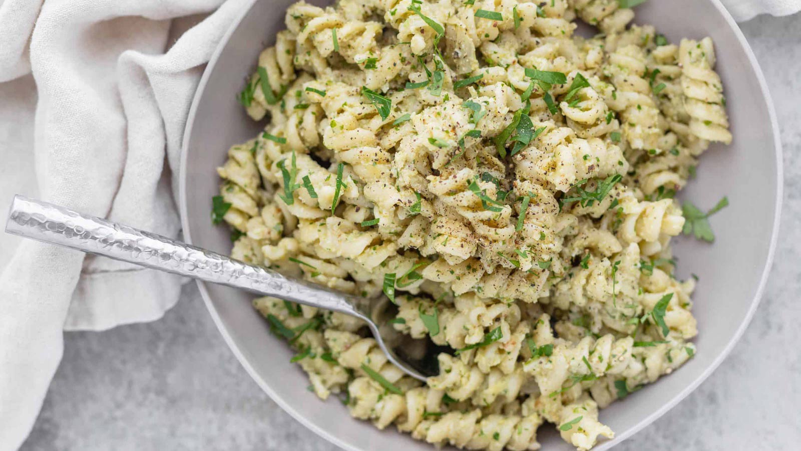 An overhead view of a white bowl filled with artichoke pesto pasta.