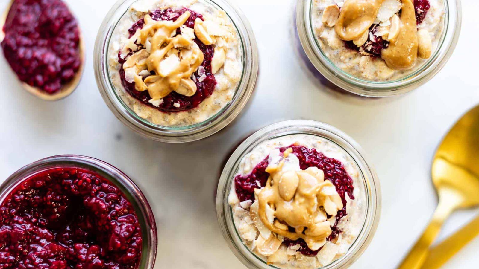 An overhead view of three jars filled with berry overnight oats with peanut butter drizzled on top.