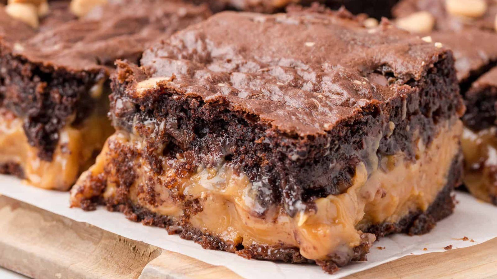 A closeup of cut brownies with a caramel layer sitting on parchment on a cutting board.